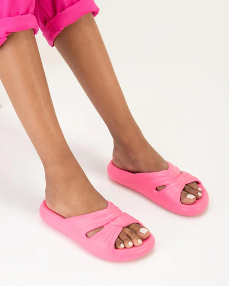 A model's legs wearing a pair of pink Melissa Free Slides with a twist front detail.