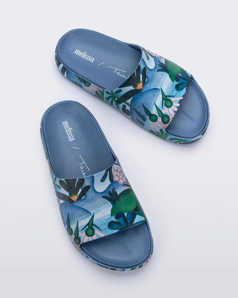 Top view of a pair of blue multicolor Melissa Cloud slides with an abstract painting design of plants, water and lagoon.