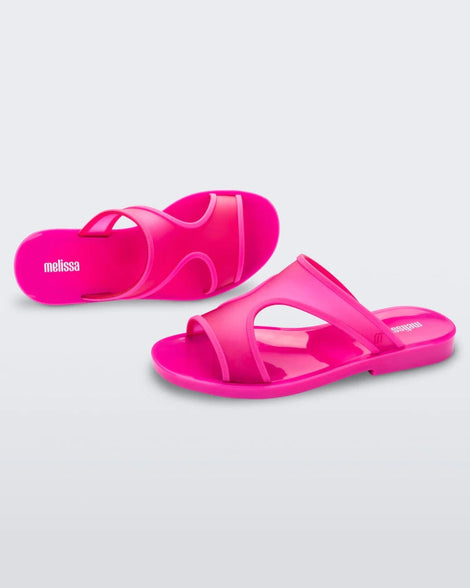 A top and side view of a pair of transparent neon pink Melissa Bikini Slides with two straps conjoining in the middle.