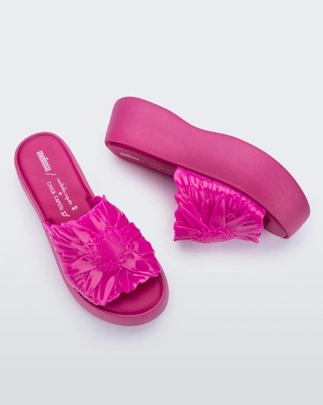 Top and side view of a pair of pink Melissa Panc Becky platform slides with a flower on top.