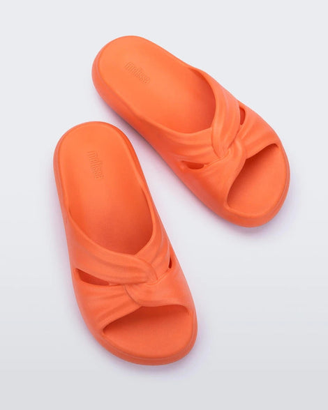 Top view of a pair of orange Melissa Free Slides with a twist front detail.