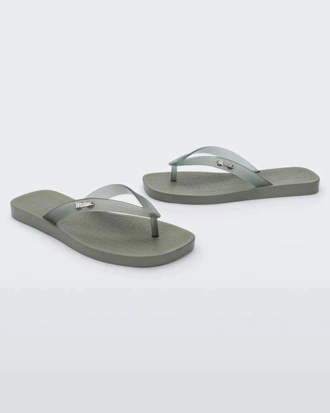 An angled front and side view of a pair of green/clear Melissa Sun Long Beach flip flops with a green base and clear green straps with 