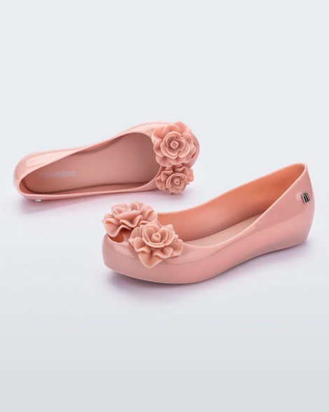 An angled side and top view of a pair of light pink Mini Melissa Ultragirl Garden flats with two rose details on the toe.