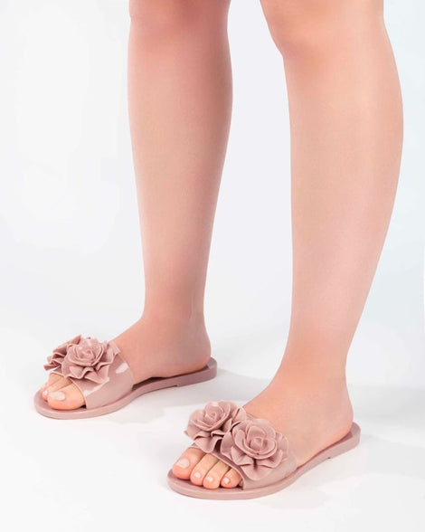 A model's legs wearing a pair of light pink Melissa Babe Garden slides with two flowers on the front strap.