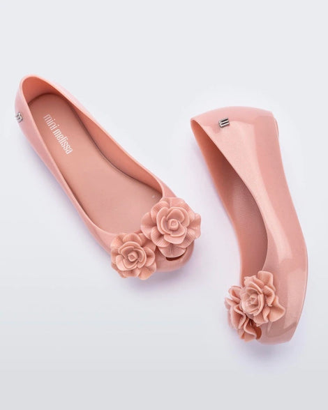 A side and top view of a pair of light pink Mini Melissa Ultragirl Garden flats with two rose details on the toe.