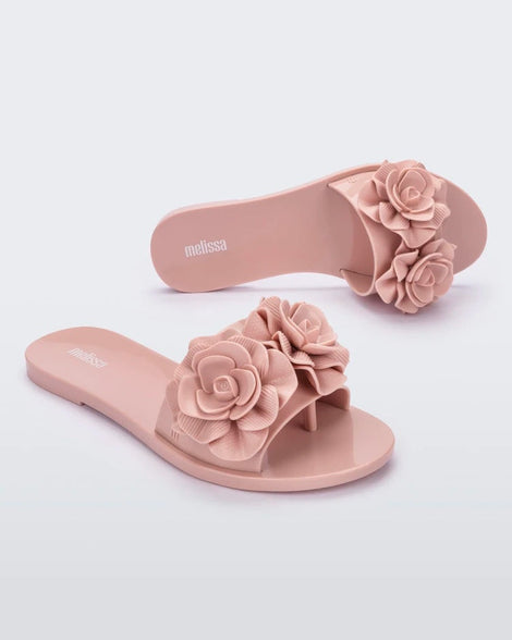 An angled top and side view of a pair of light pink Melissa Babe Garden slides with two flowers on the front strap.