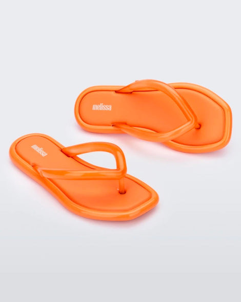 Angled view of a pair of orange Melissa Airbubble Flip Flops.