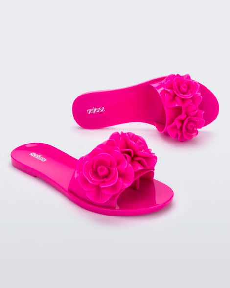 An angled side and top view of a pair of neon pink Melissa Babe Garden slides with two flowers on the front strap.