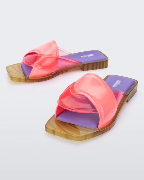 An angled front and side view of a pair of pink/green/lilac Melissa Brigitte slides with a pink weft designed upper strap and purple and green insole.