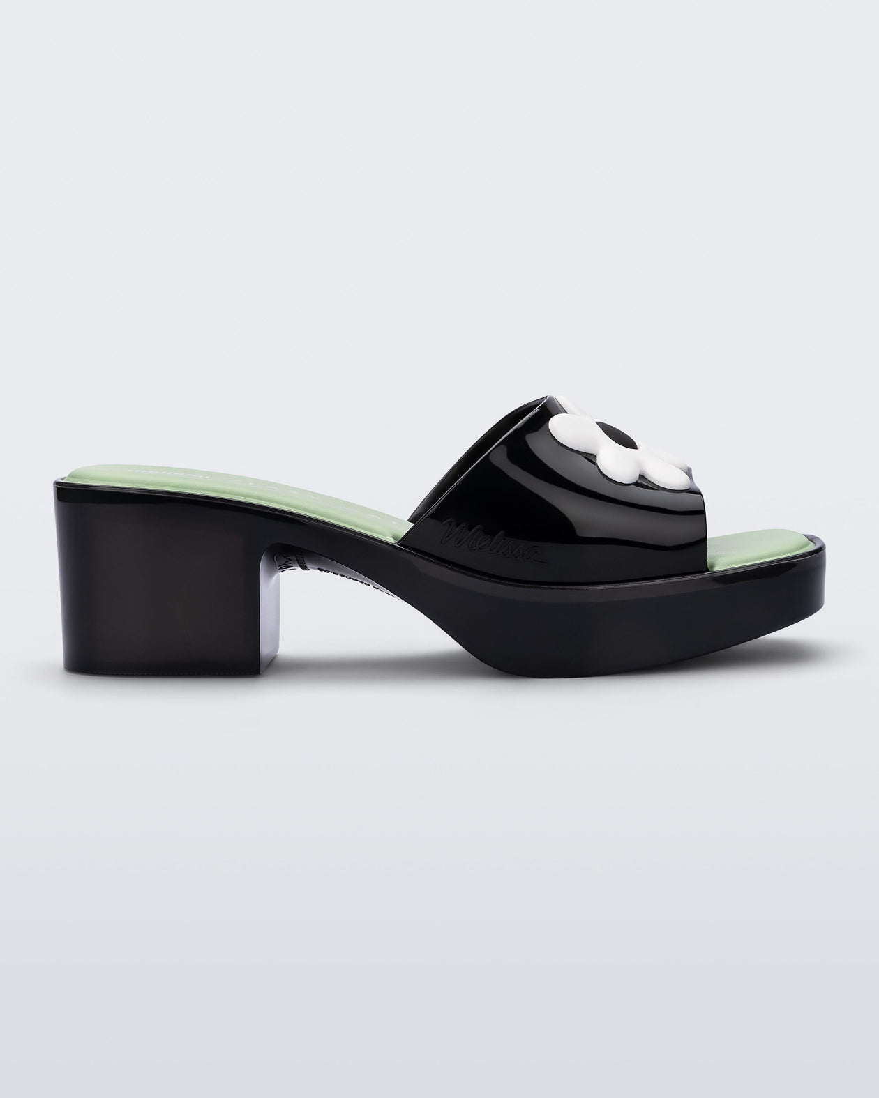 Side view of a Melissa Shape slide sandal in black with platform heel, black front strap with white flower detail and a green insole. 