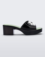 Side view of a Melissa Shape slide sandal in black with platform heel, black front strap with white flower detail and a green insole. 