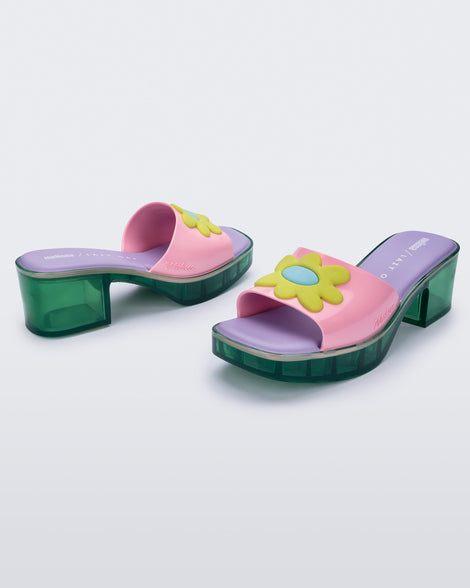 Angled view of a pair of Melissa Shape slides with green platform heel,  a pink wide front strap with a yellow and blue flower on the top of the strap and a purple insole