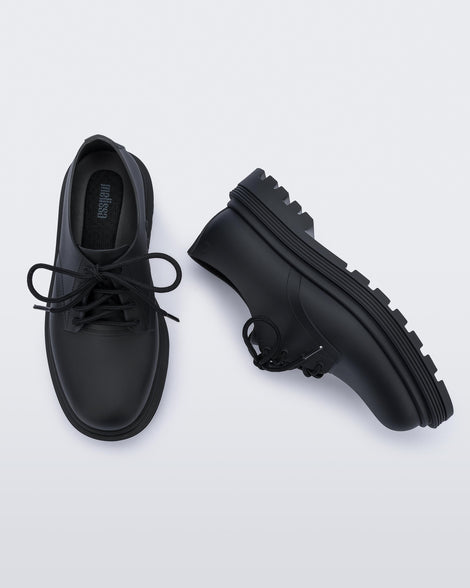 A top and side view of a pair of matte black Melissa Bass sneakers, with a black base, laces and sole.