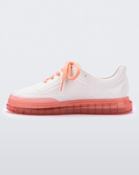 An inner side view of a pair of white Melissa Classic sneakers with a white base, laces, orange sole and a melissa logo on the side.