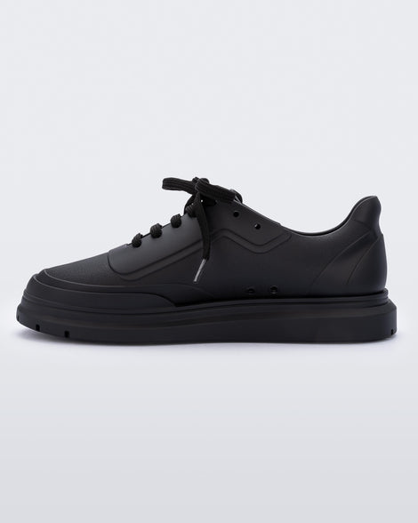 An inner side view of a matte black Melissa Classic sneaker with a black base, laces, sole and a melissa logo on the side.