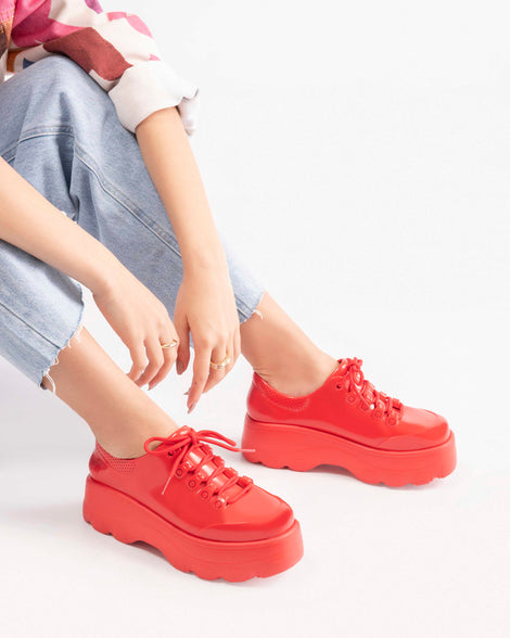 A model's legs wearing a pair of Melissa Kick Off sneakers in red with platform sole and red shoe laces 