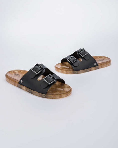 Angled view of a pair of Melissa Wide Slide sandals with gold speckled sole and two black front straps