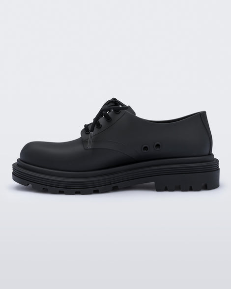 An inner side view of a matte black Melissa Bass sneaker, with a black base, laces and sole.