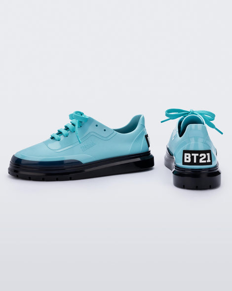 A side and back view of a pair of blue Melissa Classic sneakers with a blue base, laces, black sole, a melissa logo on the side and a BT21 black and white logo on the back.