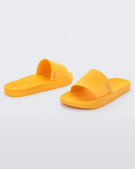 An angled front and back view of a pair of yellow Melissa Sun Sunset slides with a melissa logo on the side.