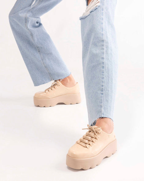 A model's legs wearing a pair of jeans and a pair of beige platform Melissa Kick Off Sneakers with laces.